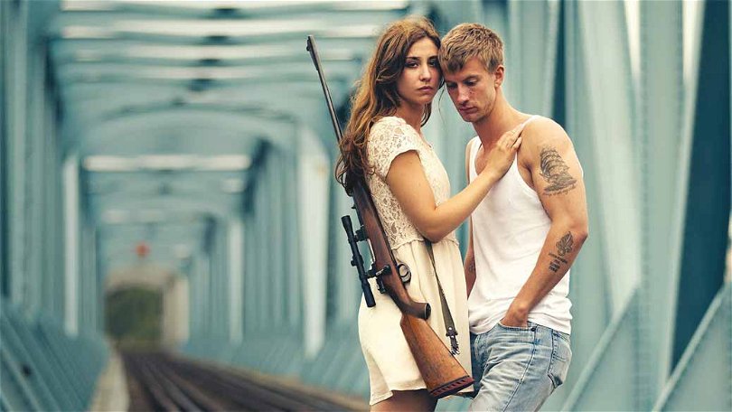 Paret i de odödliga står och håller om varandra. Kvinnan har ett gevär hängande på sin rygg.
