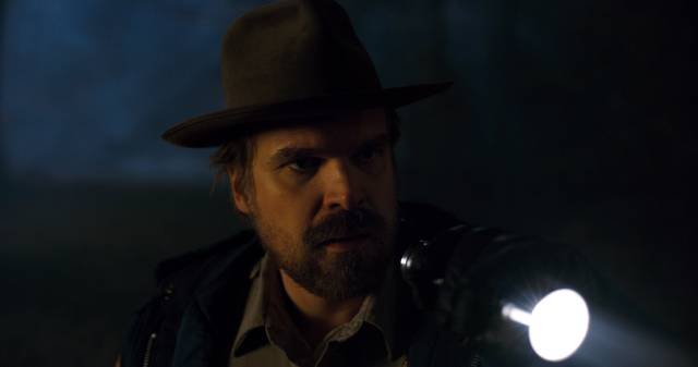 David Harbour, i rollen som Chief Jim Hopper, spanar runt i mörkret med en ficklampa.