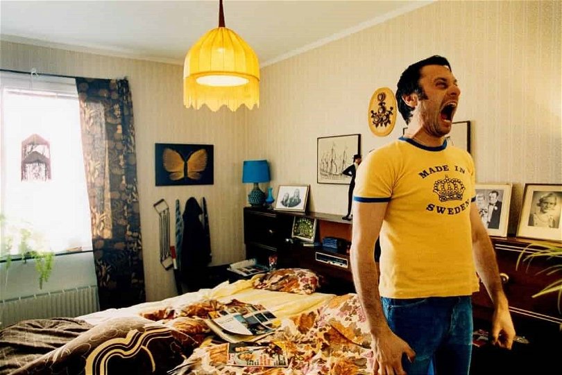Michael Nyqvist står i en lägenhet, iklädd en gul t-shirt, och skriker i "Tillsammans".