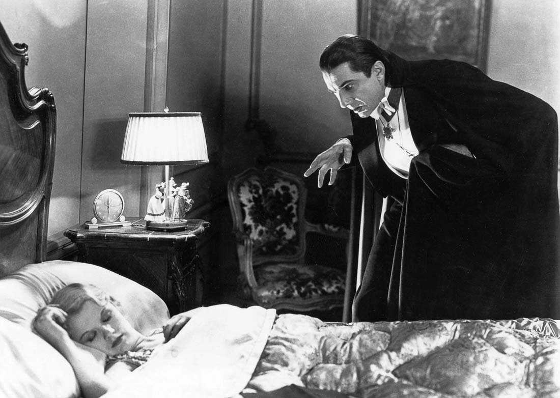 Bela Lugosi står som Dracula lutande över en kvinna som sover.