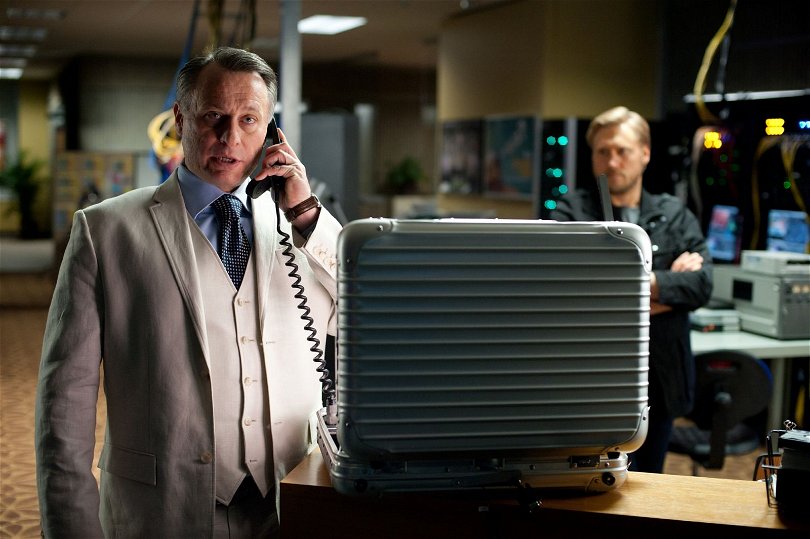 Michael Nyqvist i Mission: Impossible - Ghost Protocol. Han talar i telefon med en öppen portfölj framför sig.