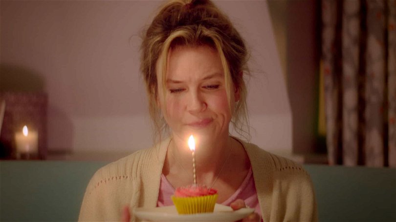 Bridget Jones sitter och firar sin födelsedag själv med en cupcake med ett ljus i.