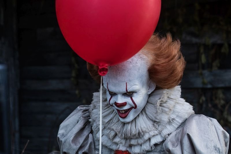 Bill Skarsgård som clownen Pennywise i skräckthrillern Det. En röd ballong svävar framför honom.