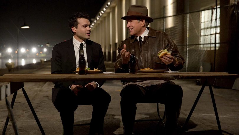 Frank (Alden Ehrenreich) och Howard Hughes (Warren Beatty) sitter på en pir vid ett bord och äter hamburgare i Rules Don't Apply. 