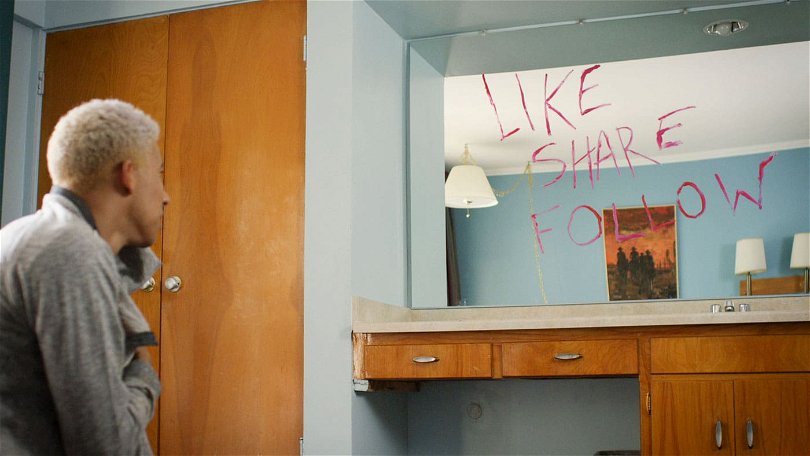 Från filmen "Like.Share.Follow". Garret tittar på en spegel där någon har skrivit Like.Share.Follow med röda bokstäver. 