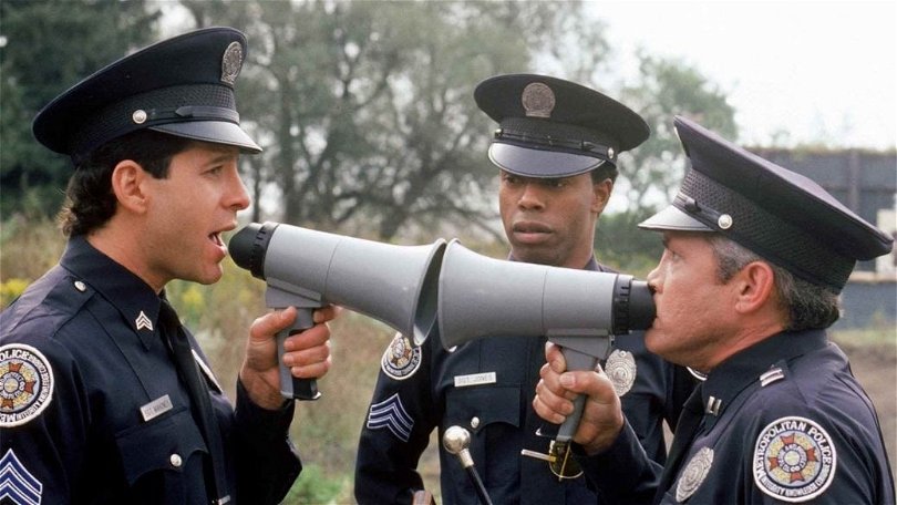 På bilden ser du två poliser ur polisskolan som skriker åt varandra i megafon.