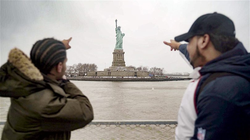 En bild ifrån HBO-dokumentären Liberty: Mother of Exiles. Bilden föreställer två unga man pekandes på frihetsgudinnan i bakgrunden. 