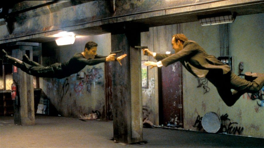 Neo (Keanu Reeves) och Agent Smith hoppar mot varandra med pistoler i händerna. Foto: Warner Bros. Pictures.
