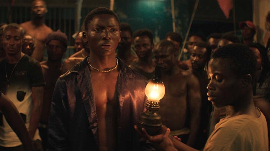 Mitt i bilden står skådespelaren Bakary Koné  i rollen som berättaren Roman i filmen Night of the Kings. Bakom honom ett antal fångars som lyssnar. 