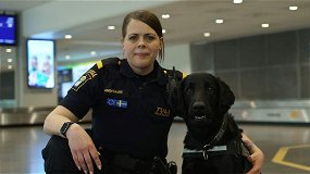 En kvinnlig hundförare står på knä bredvid en polishund.